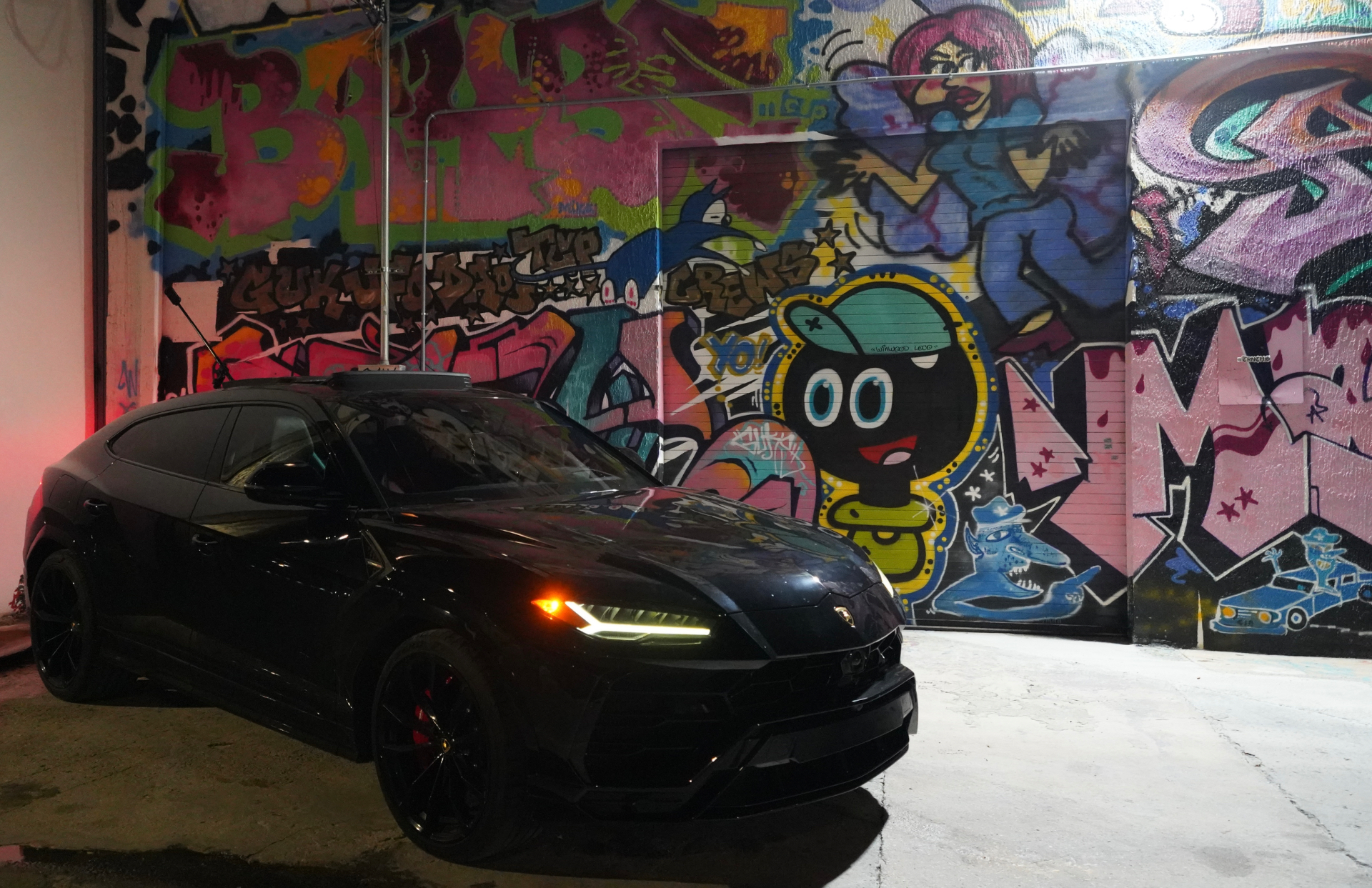 Black Lamborghini Urus in front of a colorful Miami graffiti wall at night